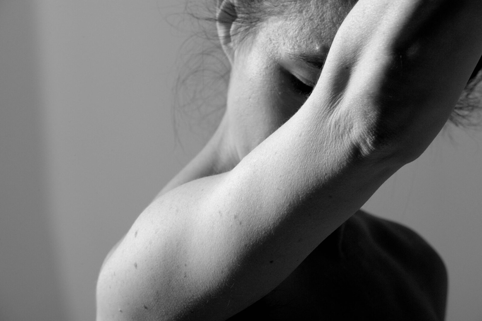 A woman with her forearm raised across her brow, eyes lowered